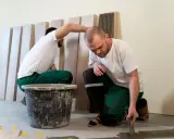 Dos obreros instalan baldosas, obra que busca repercutir mejoras al inquilino.