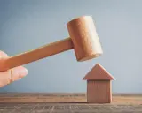 Mazo de madera a punto de golpear una casa de juguete. Posibles motivos para echar a un inquilino.