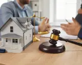 Maqueta de casa, martillo de juez y balanza de la justicia, simbolizando la ley de vivienda y disputas legales.
