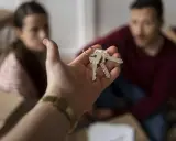 Mano entrega llaves. Pareja sonriente rodeada de cajas, lista para recuperar vivienda alquilada para un hijo.