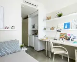Estudio moderno en residencia La Salle: cama, escritorio con lámpara y estanterías, y pequeña cocina.