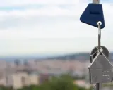 Llaves con un llavero en forma de casa, simbolizando un contrato de opción de compra. Fondo de ciudad difuminado.