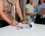 Firma de un contrato, quizás relacionado con el **artículo 32 de la ley de arrendamientos urbanos**, con llaves sobre la mesa.
