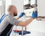 Técnico ajustando controles de caldera para bajar la presión. Herramientas en escalera.