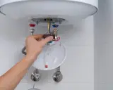 Mano ajustando el termostato de un calentador de agua, parte del proceso para saber como limpiar un termo por dentro.