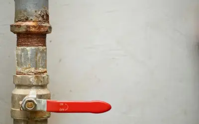 Llave de paso agua antigua, oxidada y con palanca roja, controlando el flujo.