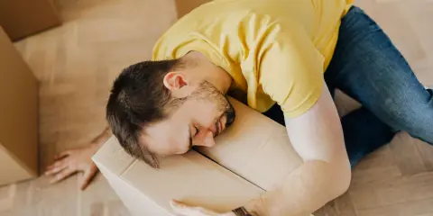 Hombre agotado durmiendo sobre una caja, quizás reflexionando sobre la diferencia entre comodato y precario tras una mudanza.