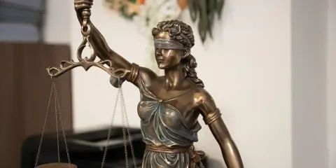 Estatua de la Justicia con venda y balanza, símbolo de imparcialidad. El texto "250.2 lec." aparece sutilmente.
