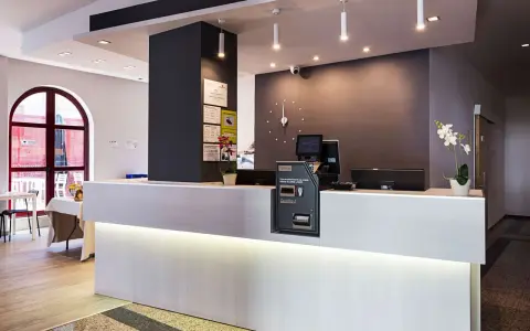 Recepción moderna y luminosa de la residencia Nuevo Versalles, con mostrador blanco, pantalla y máquina de efectivo.