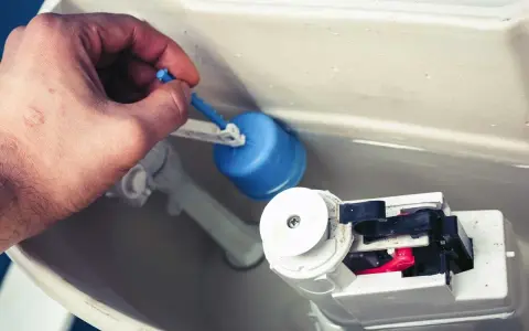 Mano ajusta el flotador azul de la cisterna, solucionando la fuga.