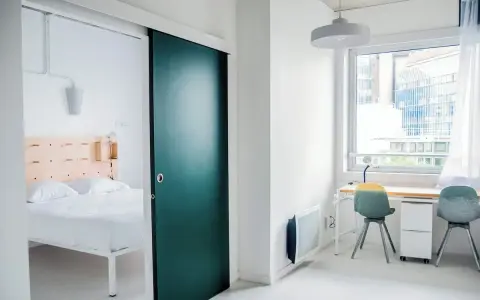 Habitación moderna con cama y escritorio. La puerta corredera verde es un detalle llamativo en este espacio, como un ecla noisy le grand.