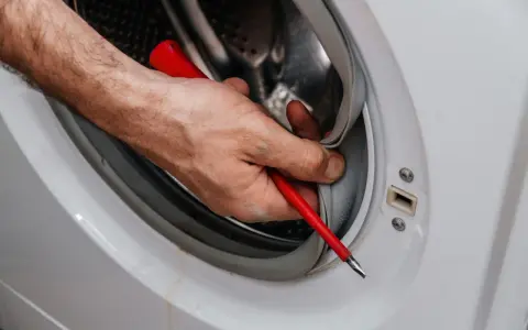 Mano con destornillador limpiando la goma de la lavadora. Aprende como quitar el moho de la goma de la lavadora para un mejor lavado.