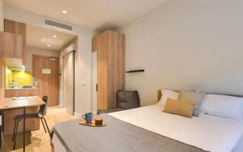 Habitación moderna con cama, escritorio y cocina. Descubre los livensa living precios para tu estancia.