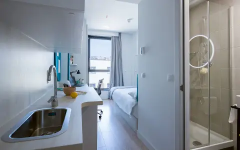 Cocina y baño moderno en residencia Garbi. Habitación con cama, escritorio y ventana.