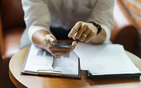 Hombre revisa su móvil, con documentos de modelo fin de contrato de alquiler y entrega de llaves sobre la mesa.
