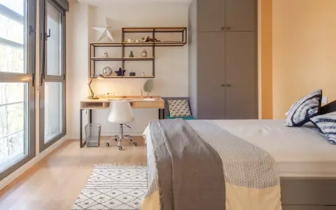 Habitación moderna en residencia San Bernardo Madrid. Escritorio, cama y armario gris. Ventanal con luz natural.