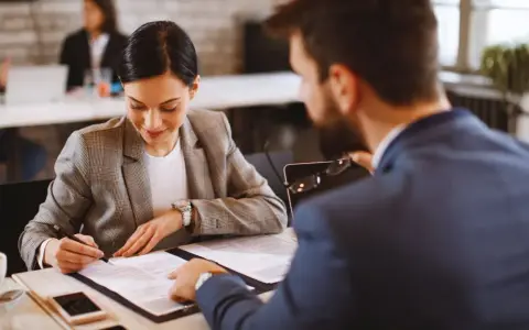 Mujer firma un precontrato de alquiler mientras un hombre revisa el documento.