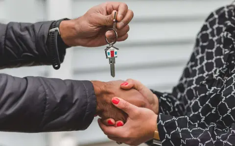 Man entrega llave de casa con llavero de hogar, mientras estrecha la mano de una mujer. Un símbolo de esperanza y fin de la suspensión de desahucios.
