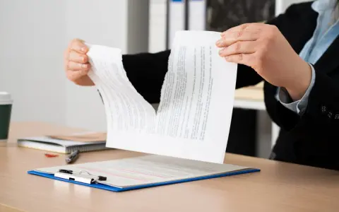 Manos rasgando un contrato, simbolizando la indemnización por incumplimiento de contrato de alquiler.