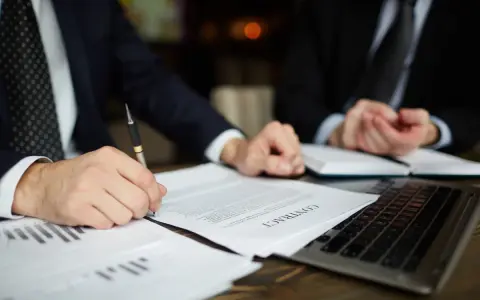 Dos hombres de negocios revisan un contrato. Uno firma el documento, mientras el otro observa. Podría tratarse de un acuerdo legal, o quizás de un proceso de embargo por impago de alquiler.