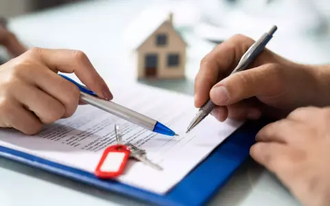 Manos firmando un documento, con llaves y una maqueta de casa. Podría ser un desistimiento de contrato de alquiler.