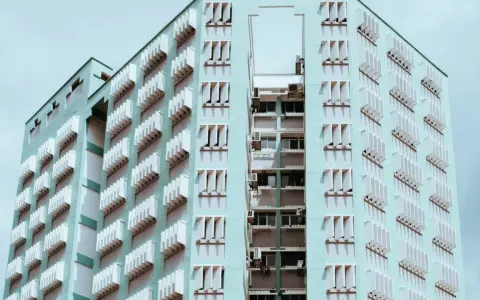 Edificio de apartamentos de color menta con filas de ventanas y persianas blancas. Un recordatorio de que se puede echar a un inquilino por necesitar el piso.