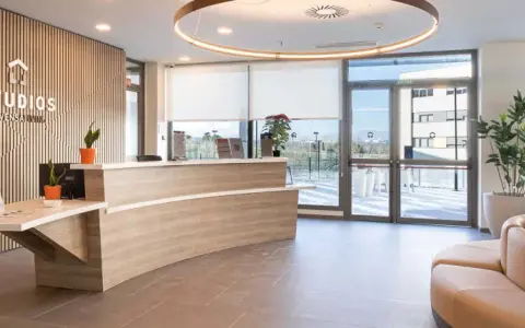 Recepción moderna y luminosa de living studios Alcobendas, con mostrador curvo, plantas y un sofá curvo.
