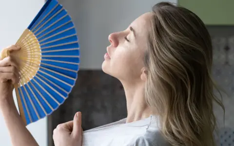 Mujer abanicándose para refrescarse, una solución para como ventilar una habitación sin ventana y combatir el calor.