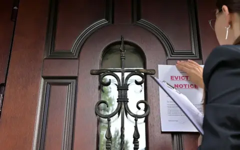 Mujer coloca un aviso de desalojo en una puerta de madera. Proceso para como echar a un inquilino sin contrato.