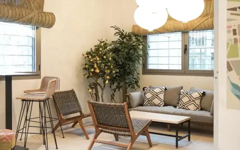 Un espacio acogedor con sofá, sillones de mimbre y un limonero, ideal para relajarse en los lumiere apartamentos.