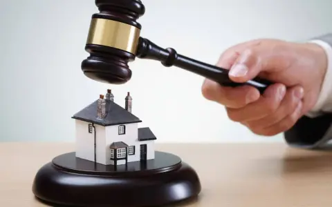 Martillo de juez golpea una casa en miniatura. ¡Qué mala suerte si estoy de alquiler y el piso sale a subasta!