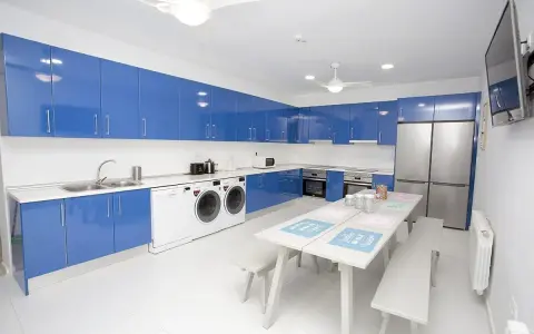 Cocina moderna con armarios azules brillantes, electrodomésticos y una mesa para compartir. Un espacio ideal para una **student factory** donde convivir y estudiar.