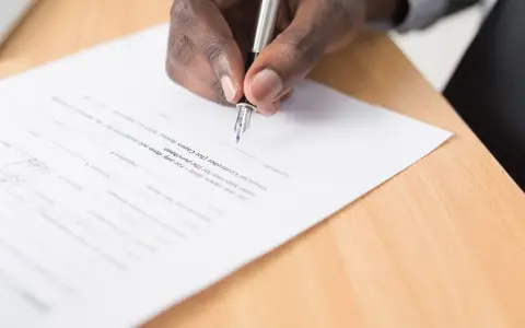 Mano firmando un documento, cumpliendo con el artículo 6 de la LAU, que requiere aprobación para la compra.
