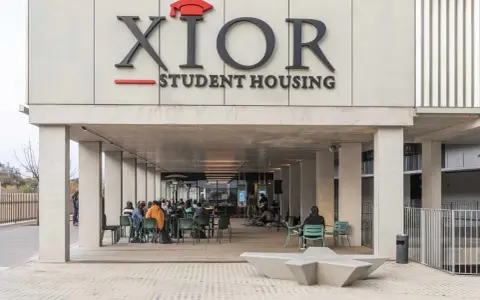 Estudiantes disfrutan en la **residencia Xior Picasso-Velázquez**. Un grupo toca música en vivo mientras otros charlan y comen al aire libre.