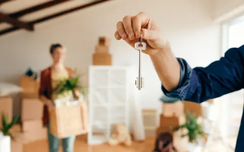 Mano sostiene llave de piso. Mudanza con cajas y planta. ¡Cuidado! Te pueden echar de un piso de alquiler sin contrato.