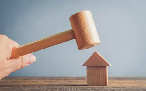Mazo de madera a punto de golpear una casa de juguete. Posibles motivos para echar a un inquilino.