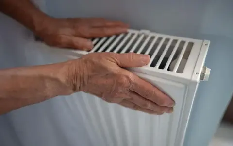 Manos sobre un radiador blanco, sintiendo el calor. Quizás se pregunte porque suenan los radiadores.