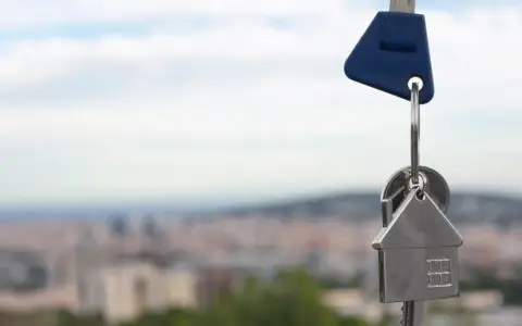 Llaves con un llavero en forma de casa, simbolizando un contrato de opción de compra. Fondo de ciudad difuminado.