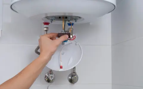 Mano ajustando el termostato de un calentador de agua, parte del proceso para saber como limpiar un termo por dentro.