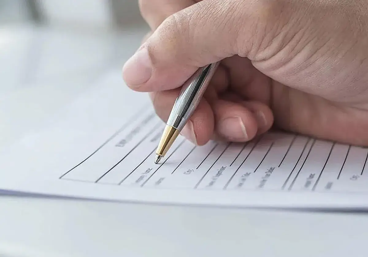 Mano firmando un contrato de arrendamiento con bolígrafo plateado y dorado.