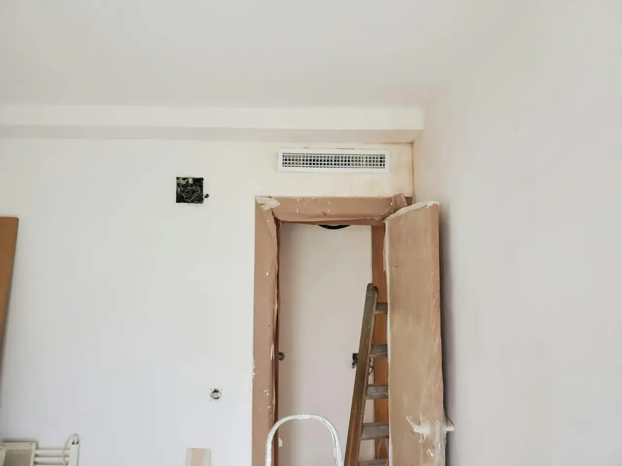 Habitación en obra con rejilla de preinstalación aire acondicionado en la parte superior de la puerta. Escalera y materiales de construcción.