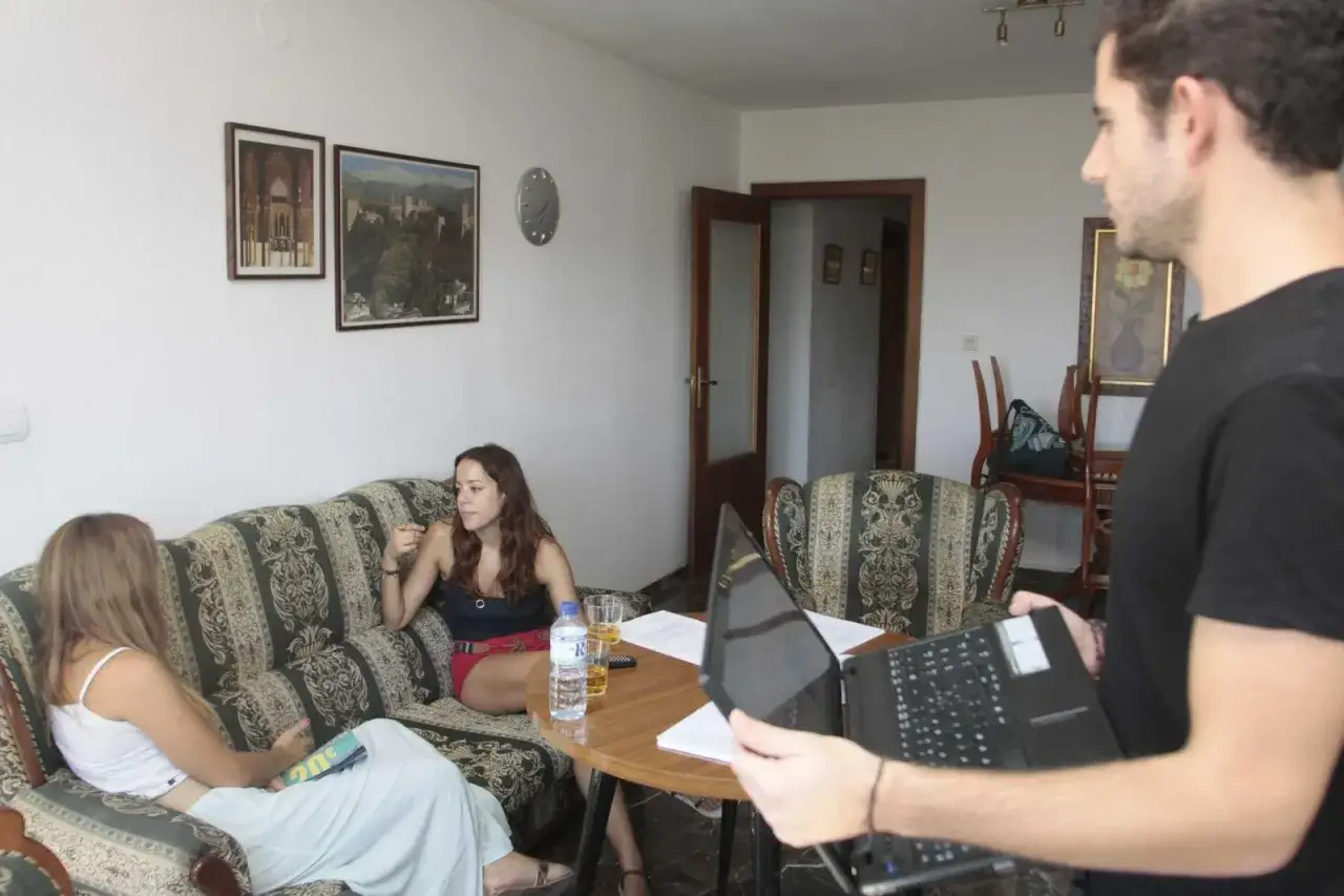Un hombre con un portátil se acerca a dos mujeres sentadas en un sofá, discutiendo el articulo 4 lau.