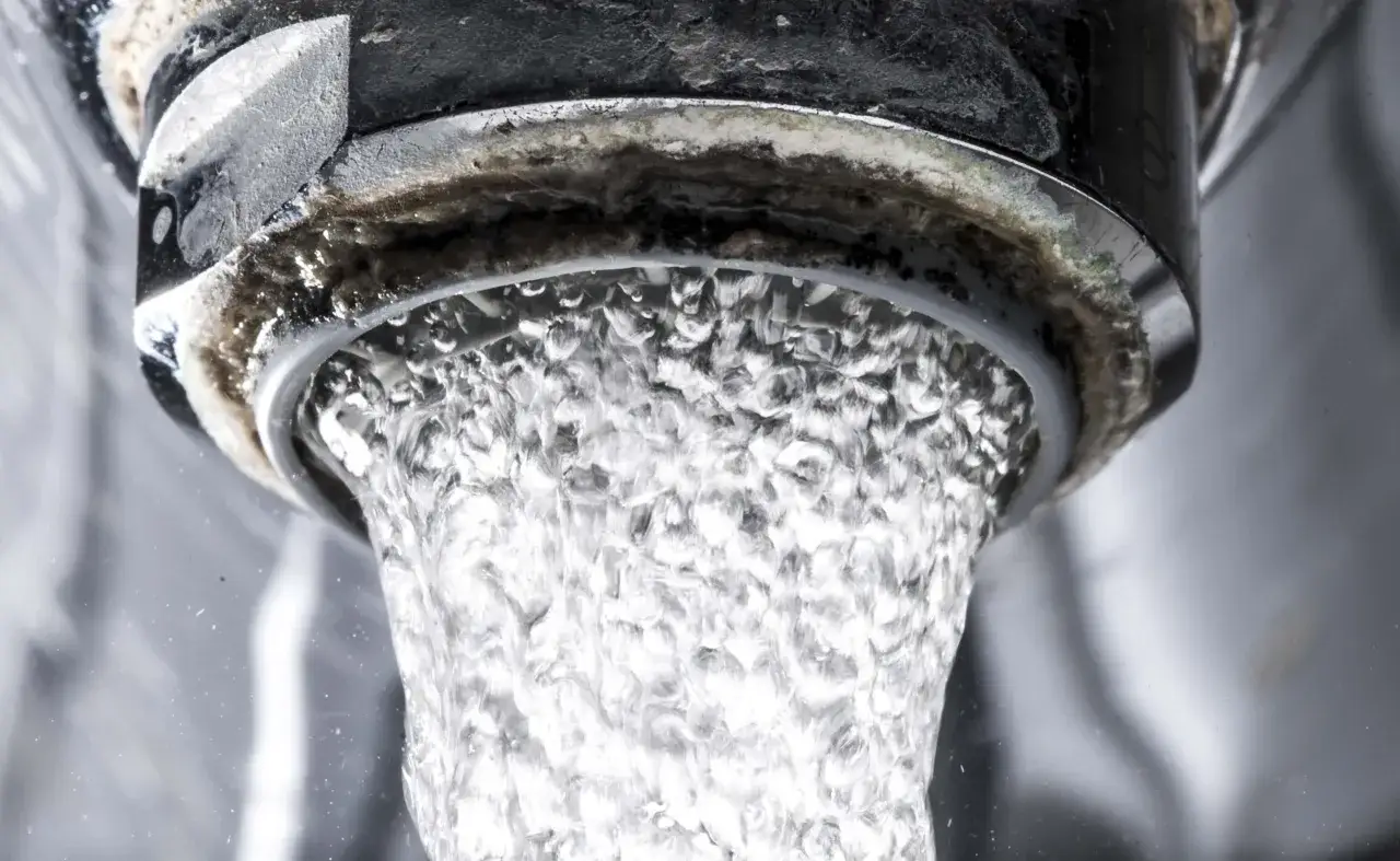 Agua fluyendo de un grifo con acumulación de cal en las tuberías.