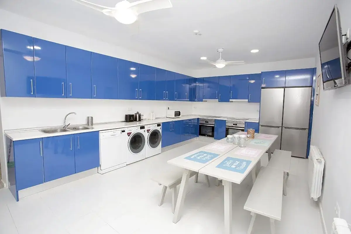 Cocina moderna y funcional en una residencia estudiantil, con armarios azules brillantes, electrodomésticos y una mesa para compartir.