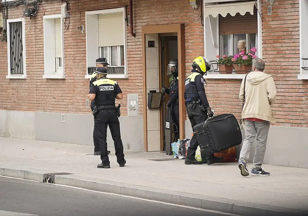 Policías intervienen en una vivienda. Un hombre arrastra una maleta, mientras una mujer observa desde la ventana. Podría ser una escena de suspensión de desahucios.