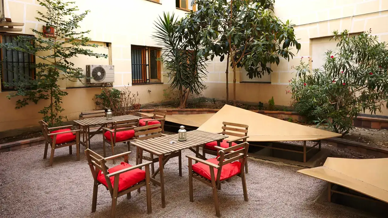 Patio acogedor con mesas y sillas de madera con cojines rojos, ideal para relajarse en la residencia San Bernardo Madrid.