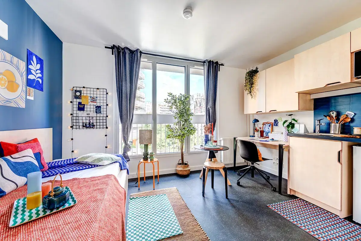 Habitaci&oacute;n moderna con cama, escritorio y cocina. Un gran arco de luz ilumina el espacio, creando un ambiente acogedor.