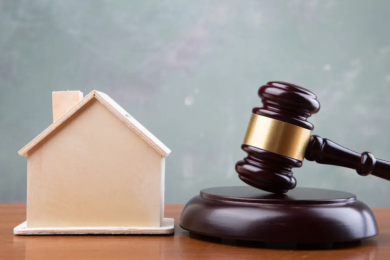 Martillo de juez junto a una casa de madera, simbolizando la ley Boyer y las decisiones sobre propiedades.