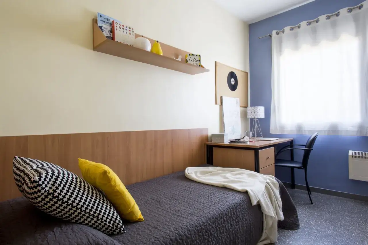Habitación de estudiante en la carlos v residencia granada. Cama, escritorio con lámpara y ventana.