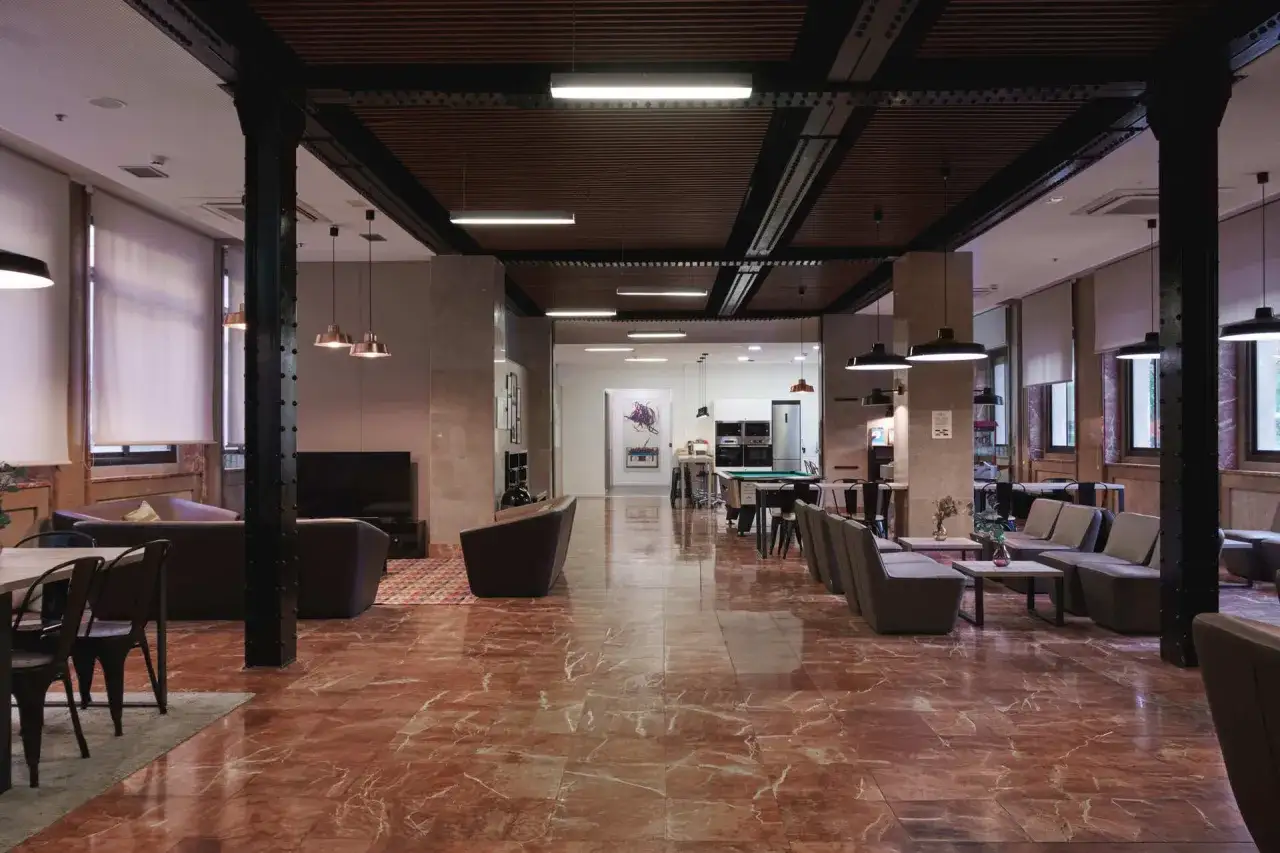 Amplio salón de la residencia diagonal con suelo de mármol rojo, sofás, mesas y zona de juegos.